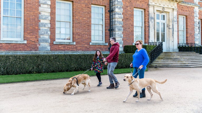 Two adults and a child with two dogs on leads in front of a red bricked hall